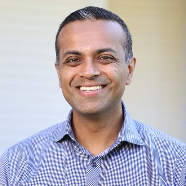 Amar Kumar smiling warmly while wearing a checkered shirt against a softly blurred background.