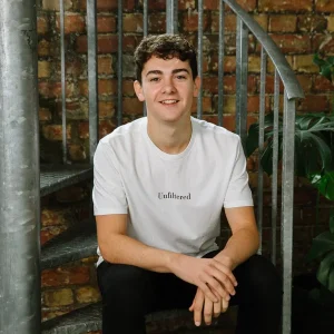 Ben Towers sitting on a spiral staircase, wearing a white shirt and smiling.