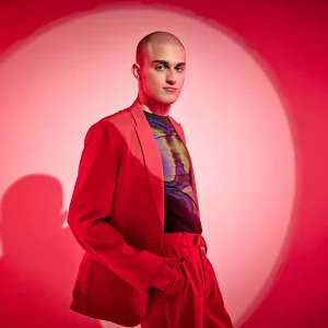 Christopher El Badaoui in a bold red suit posing confidently against a bright circular backdrop.