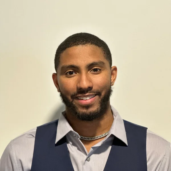 Colby Harvey smiling in a light gray shirt and dark vest against a plain background.