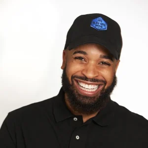 Smiling DéVon Christopher Johnson wearing a black cap and black polo shirt against a plain background.