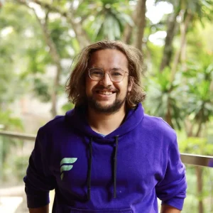 Smiling James da Costa with glasses and long hair wearing a purple hoodie outdoors.