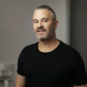 Jason Goldberg with short gray hair and beard wearing a black shirt in a dim room.