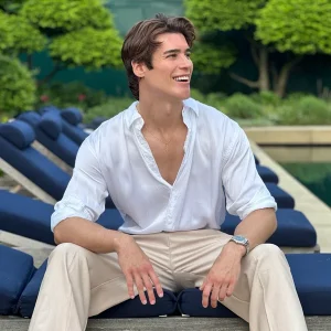 José “JJ” Martín Quesada sitting on a poolside lounge chair, smiling while wearing a white shirt