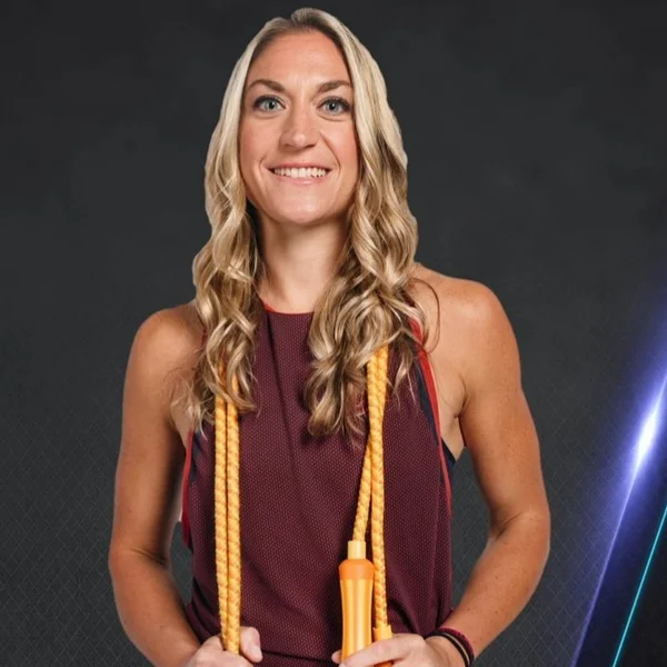 Smiling Lauren Foundos with long blonde hair holding a yellow jump rope against dark background.