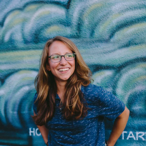 Lindsey Lerner smiling while standing in front of a blue mural with swirling wave patterns.
