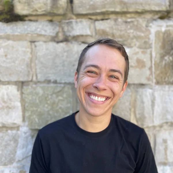 Smiling Luke Lennon in a black shirt standing in front of a stone wall.
