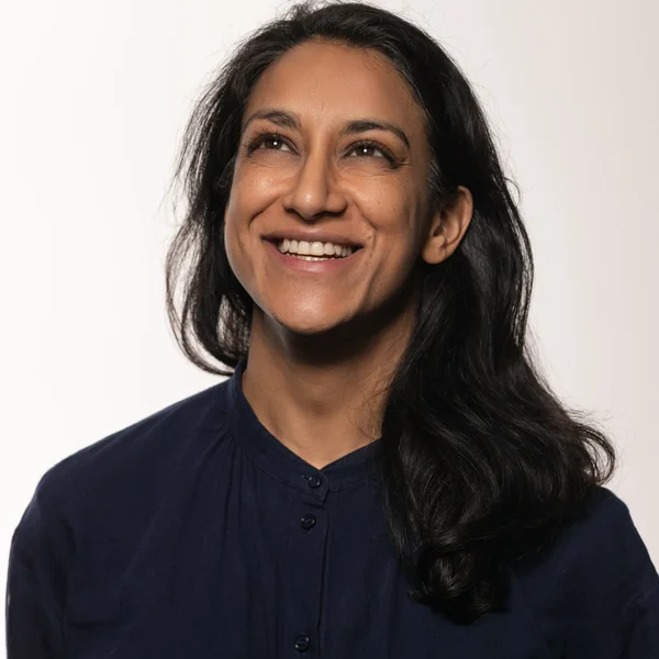 Mandeep Soor smiling and looking upward while wearing a dark top against a light background.