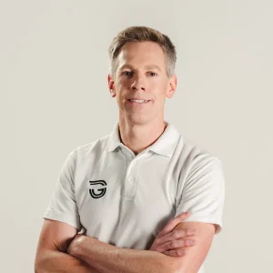 Mark Seeger in a white polo shirt with folded arms standing against a plain background.