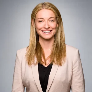 Melissa Kozak smiling in a light blazer and dark top against a neutral gray background.