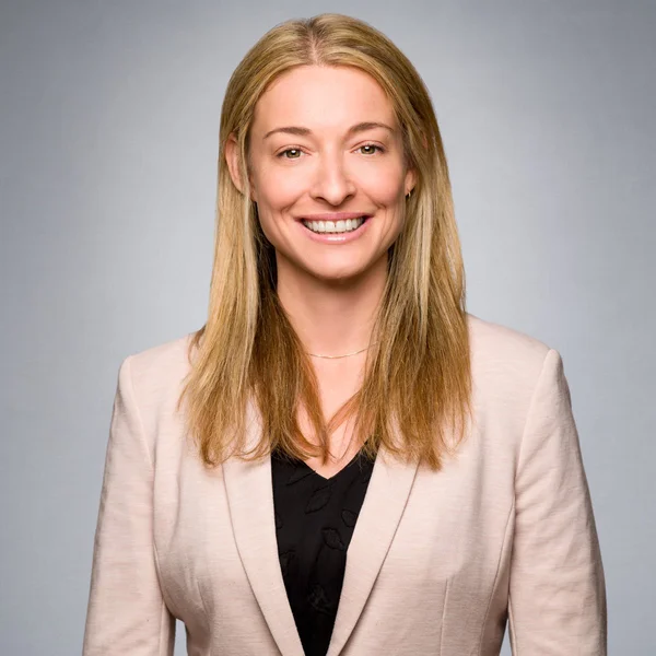 Melissa Kozak smiling in a light blazer and dark top against a neutral gray background.