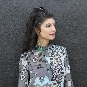 Olivia Hayes in a patterned blouse looking to the side against a textured dark wall.