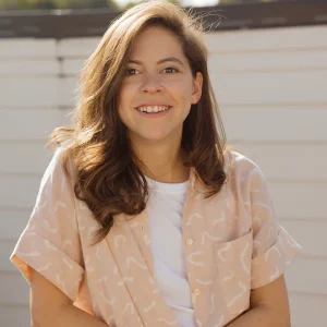 Smiling Rachel Renock with wavy hair wearing a light patterned shirt and white T-shirt outdoors.