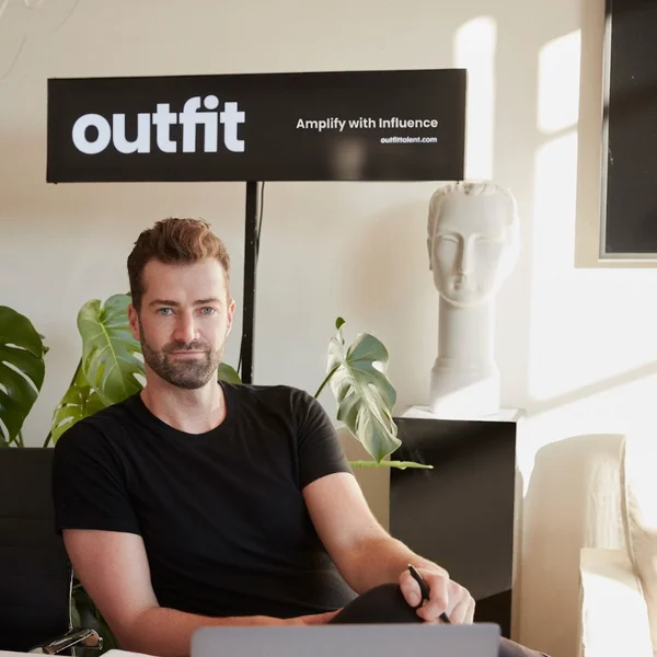 Ryan Mulcock seated at a desk in a bright office with plants and a company sign.