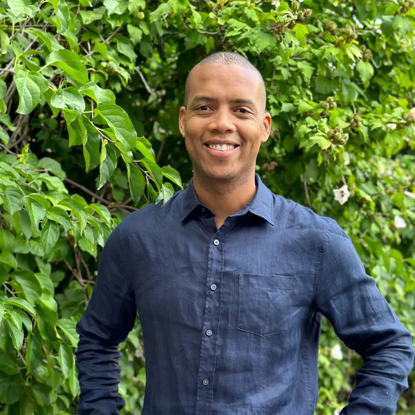 Vince McPhillip smiling outdoors while standing in front of lush green leafy branches.