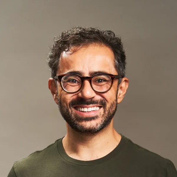 Smiling man with glasses and short curly hair posing against a plain background.