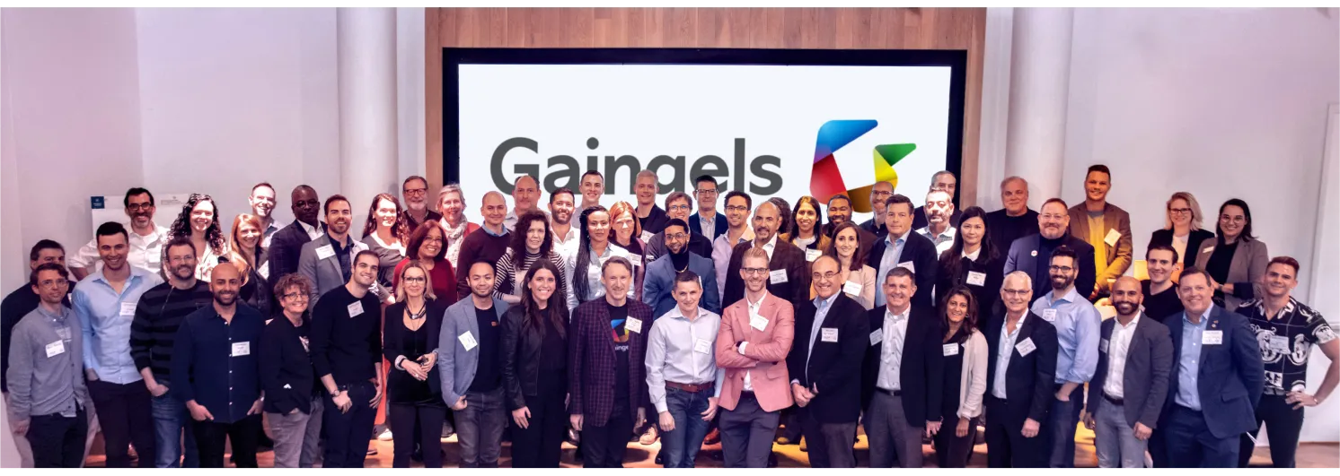 A large group of diverse professionals poses in front of a screen with the Gaingels logo.